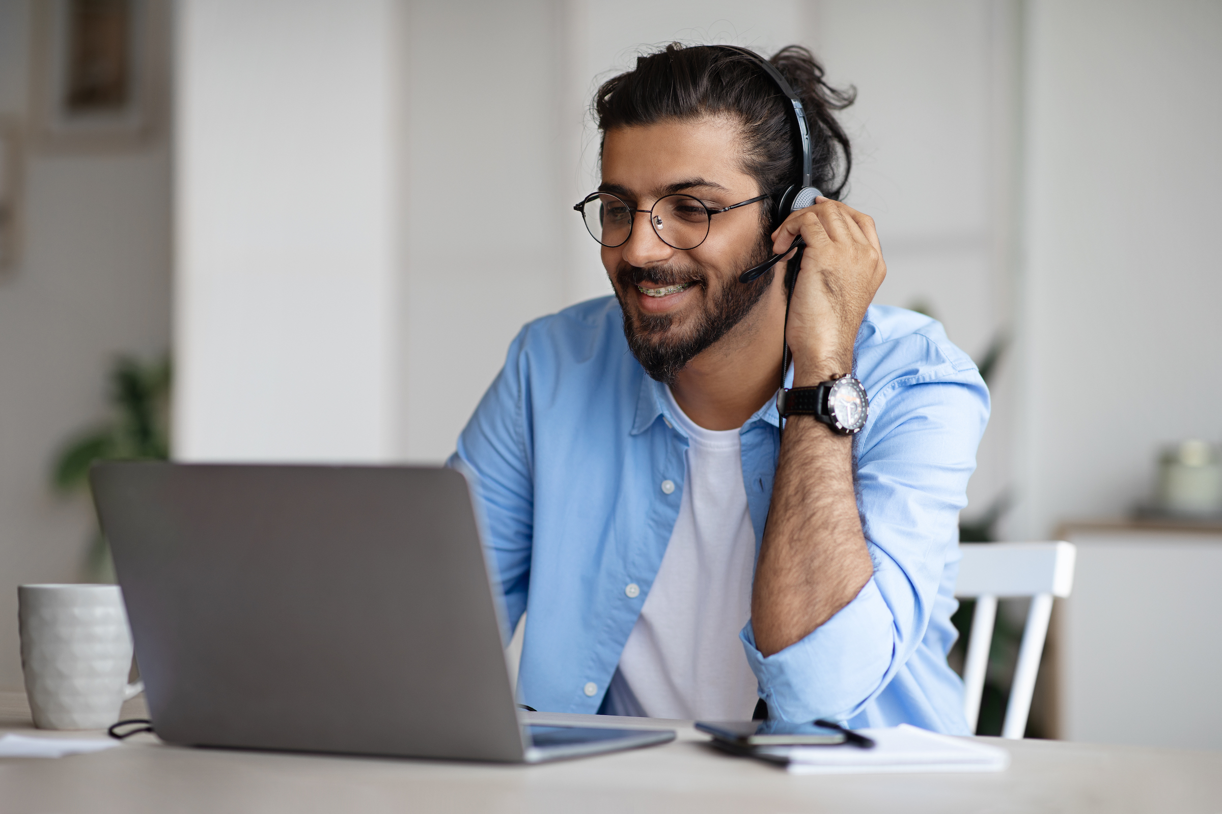 A man with a headset smiles at his laptop.