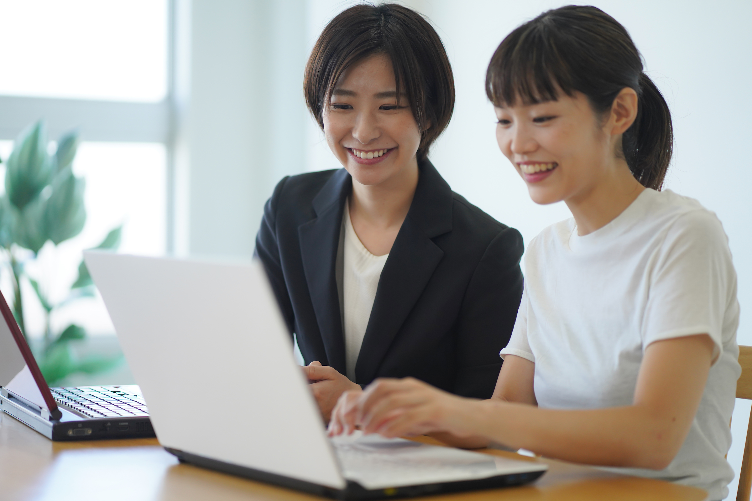 Two women sit down in front of a laptop.