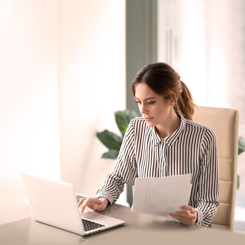 A woman sits down at her desk and examines her laptop