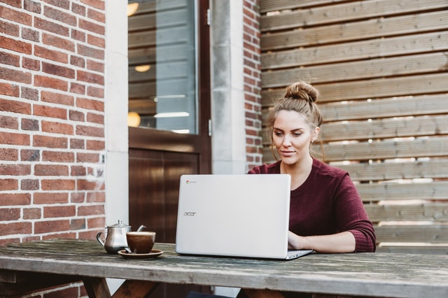 A woman sitting on a bench looking at her laptop.