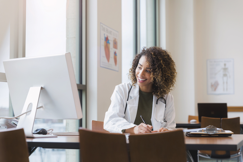 A Medical expert at her desk smiling at her computer.