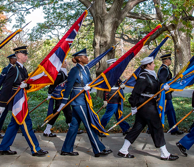 Members of the military holding flags in a procession outside.