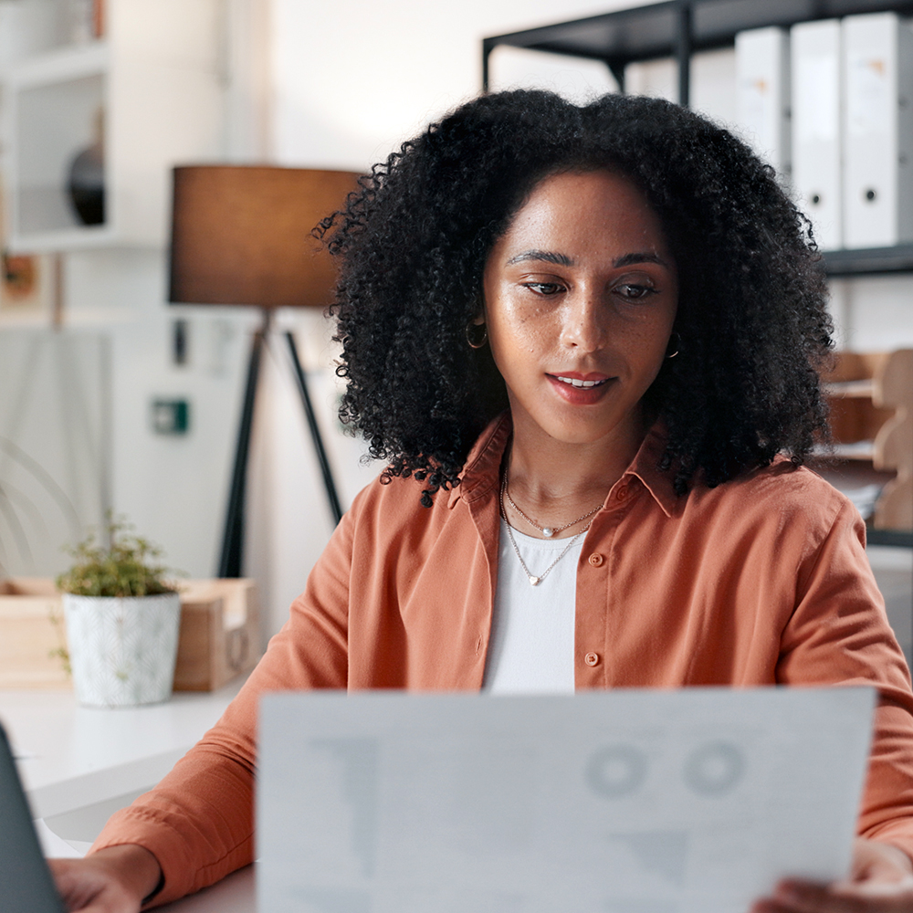Woman sitting at a desk in front of a laptop and holding a piece of paper.