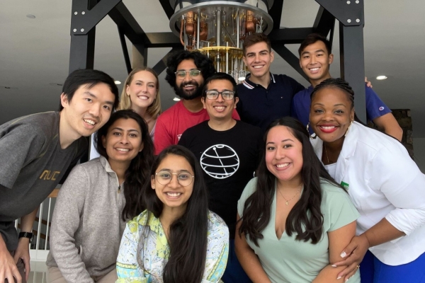 Ten members of the 2023 IBM Quantum internship class pose in front of a dilution refrigerator.
