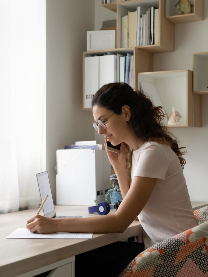 Businesswoman wearing glasses making phone call, writing notes, consulting client.