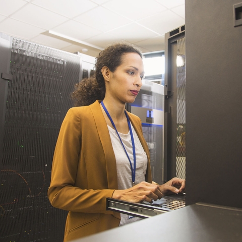 woman in server room working on laptop