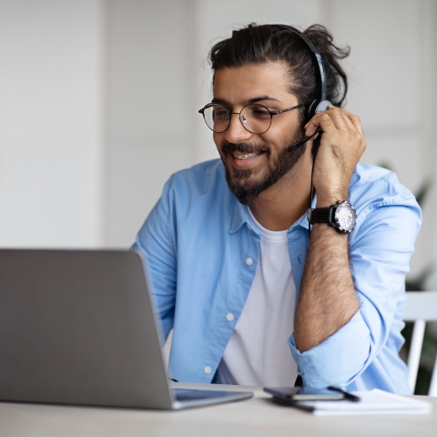 A man with a headset smiles at his laptop. 