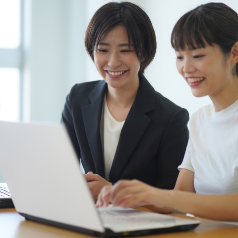 Two women sit down in front of a laptop. 