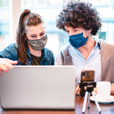 two people wearing face masks while looking at a computer screen