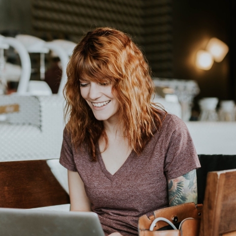 A woman smiles into her laptop at a coffee shop.