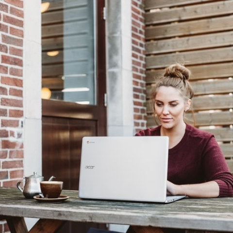 A woman sitting on a bench looking at her laptop.