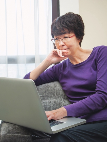 Elderly woman sitting down browsing the web on her laptop.