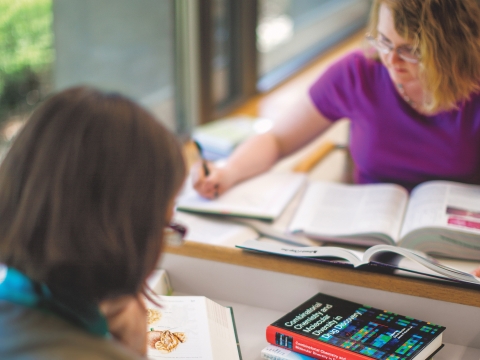Students writing at desk with books