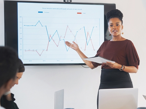 Woman standing in front of a presentation, gesturing to the screen.