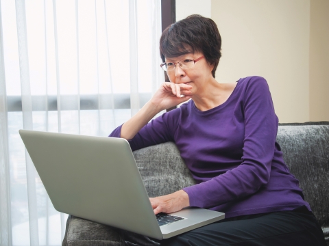 Elderly woman sitting down browsing the web on her laptop.