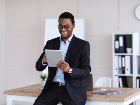 Man leaning against a desk and smiling while looking at a report.