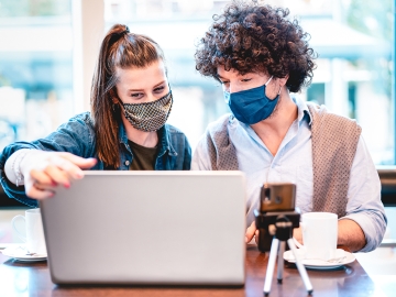 two people wearing face masks while looking at a computer screen